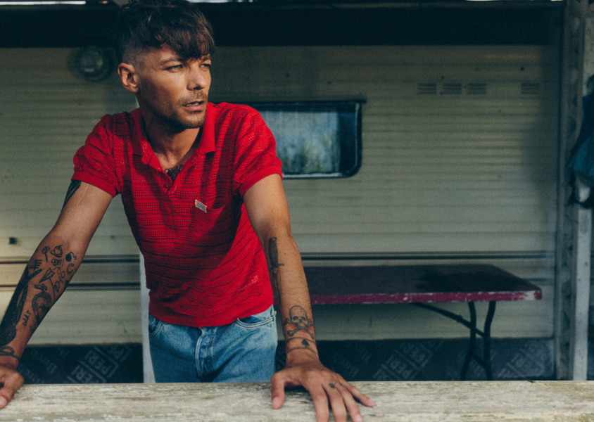 Musician Louis Tomlinson in a red top leaning on a wallx